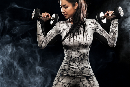Sporty beautiful woman with dumbbells makes fitness exercising at black background to stay fitの写真素材