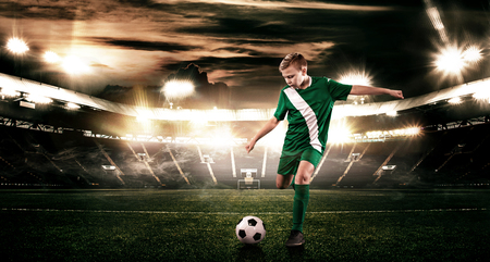 Kid - soccer player. Boy forward in football sportswear on stadium with ball. Sport concept.の写真素材