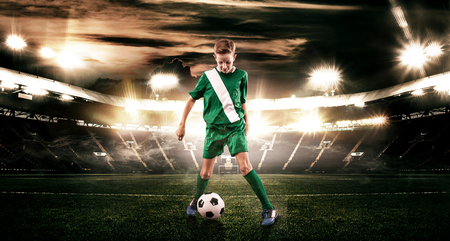 Kid - soccer player. Boy forward in football sportswear on stadium with ball. Sport concept.の写真素材