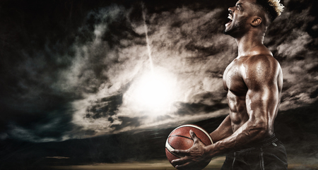 Portrait of male basketball player with a ball over black background. Fit young man in sportswear holding basketball.の写真素材