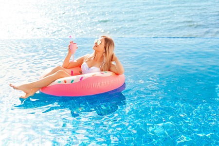 Summer Vacation. Enjoying suntan Woman in bikini on the inflatable mattress in the swimming pool with coctail.の写真素材