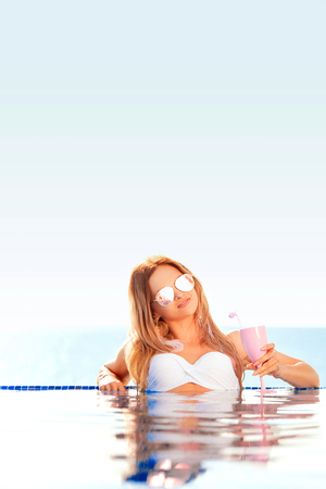 Summer Vacation. Enjoying suntan Woman in bikini on the inflatable mattress in the swimming pool with coctail.の写真素材