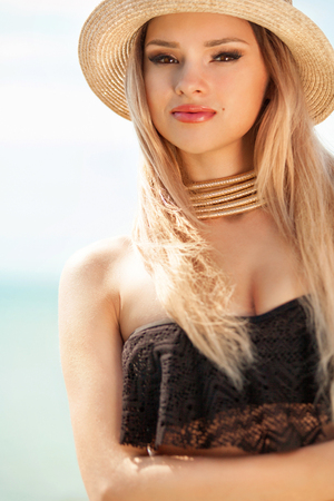 Beautiful fit woman in black swim suit and hat posing on the beach. Summer vacation.の写真素材