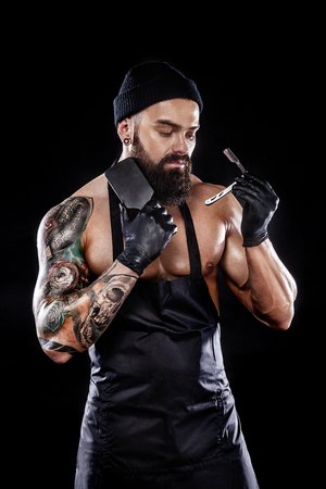 Portrait of bearded barber with a straight razor and comb with tattooe on arm. Barbershop ads concept with copy space.の写真素材