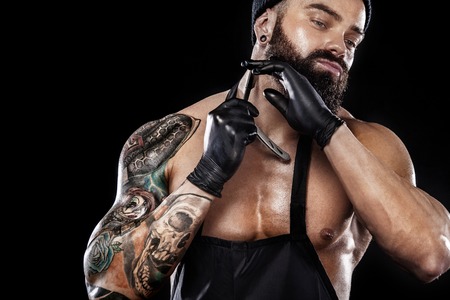 Portrait of bearded barber with a straight razor with tattooe on arm. Barbershop ads concept with copy space.の写真素材