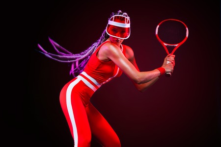 Tennis player. Beautiful woman athlete with racket in red costume and hat isolated on black background. Fashion and sport concept.の写真素材