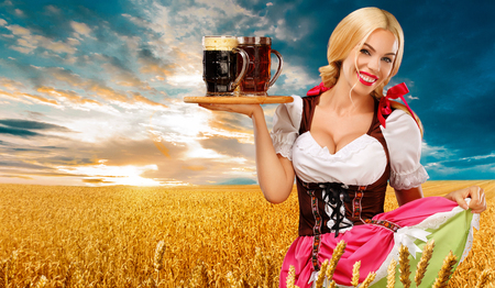 Half-length portrait of young sexy blonde with big breast wearing color dirndl with white blouse holding the beer mug Isolated on blue backgroundの写真素材