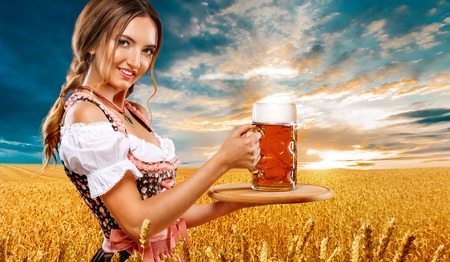 Half-length portrait of young sexy blonde with big breast wearing color dirndl with white blouse holding the beer mug Isolated on orange backgroundの写真素材