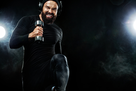 Muscular young fitness sports man, athlete workout with dumbbell and headphones in gymの写真素材
