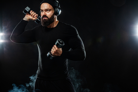 Muscular young fitness sports man, athlete workout with dumbbell and headphones in gymの写真素材