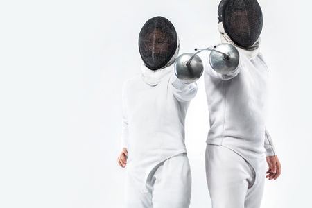 Two Young fencers athletes wearing mask and white fencing costume and holding the sword. Isolated on...