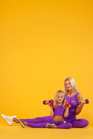 Mothers day concept. Young mother and daughter exercise together with dumbbells. Family look.の写真素材