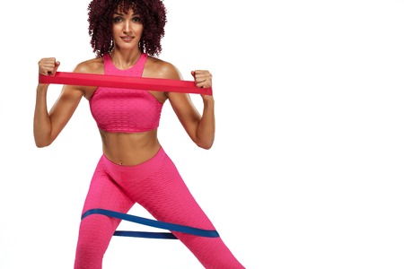 Muscular young fit sports woman athlete in pink sportswear with bands or expander in gym. Copy space for fitness nutrition ads.の写真素材