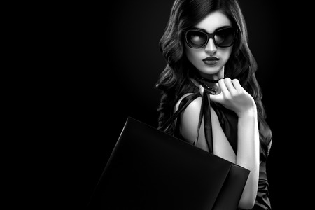 Christmas or Black friday sale concept. Shopping woman holding bag on dark background in holiday. BW photo.の写真素材