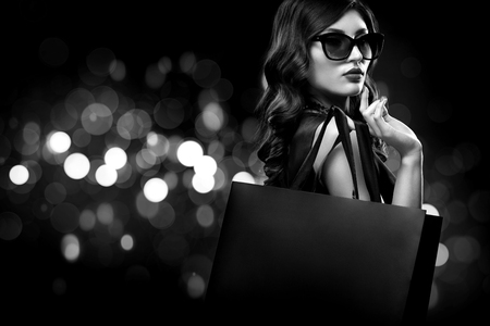 Christmas or Black friday sale concept. Shopping woman holding bag on dark background with bokeh in holiday. BW photo.の写真素材