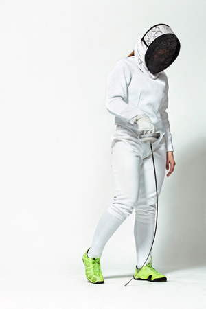 Young fencer athlete wearing fencing costume and mask holding the sword. Isolated on white...