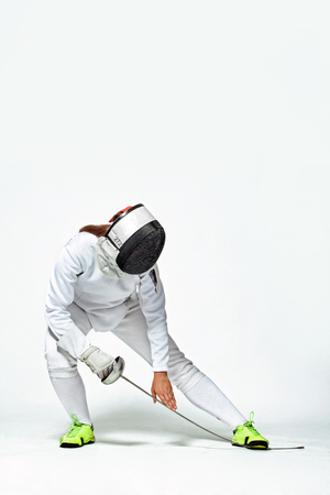 Young fencer athlete wearing fencing costume and mask holding the sword. Isolated on white backgroundの写真素材