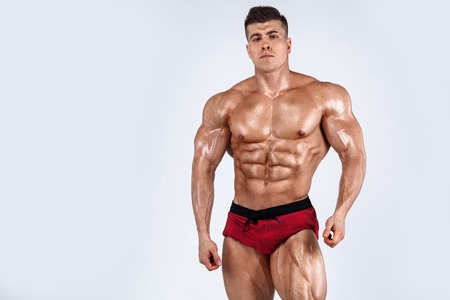 Brutal strong muscular bodybuilder athlete man pumping up muscles on white background. Workout...