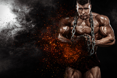 Brutal strong muscular bodybuilder athletic man pumping up muscles with chains on black background. Workout bodybuilding concept. Copy space for sport nutrition ads.の写真素材