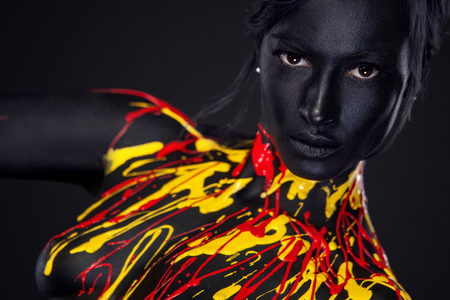 Cheerful young woman with art fashion makeup. An amazing woman with black, yellow and red paint makeupの写真素材