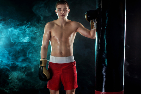 Sportsman, man boxer fighting in gloves with boxing punching bag. Isolated on black background with smoke. Copy Space.の写真素材