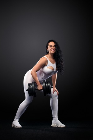 Size plus woman sporty fit woman in white sportswear, athlete with dumbbells makes fitness exercising on black background with lights. Motivation for fat people.の写真素材
