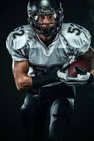 American football player, sportsman in helmet on black background with smoke. Sport and motivation wallpaper.の写真素材