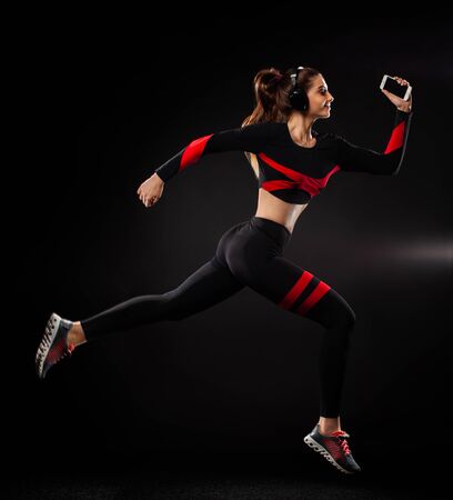 Strong athletic woman sprinter, running on black background wearing in the sportswear and headphones. Fitness and sport motivation. Runner concept.の写真素材