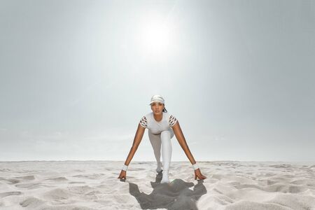 Fit woman sprinter, start running at the desert wearing in white sportswear. Fitness and sport motivation. Runner concept with copy space.の写真素材