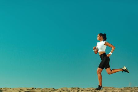 Sporty young woman and fit athlete runner running on the sky background. The concept of a healthy lifestyle and sport. Woman in black and white sportswear.の写真素材