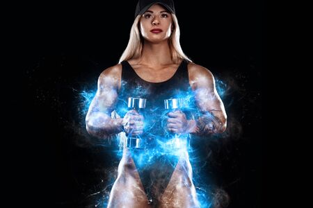 Strong athletic woman bodybuilder with dumbbells on dark background wearing in sportswear. Fitness and sport motivation.の写真素材