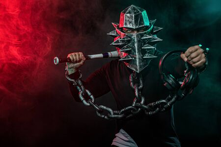 Mysterious man in a helmet with a bat and chains in black wear. Fantasy book or computer game cover...