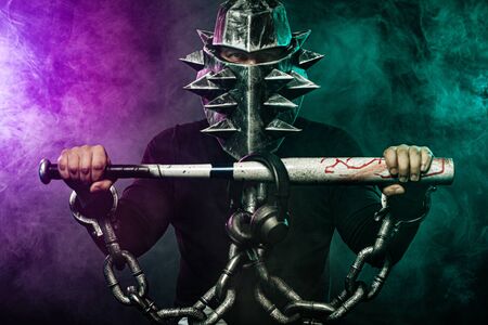 Mysterious man in a helmet with a bat and chains in black wear. Fantasy book or computer game cover...