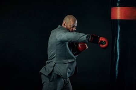Businessman and sportsman in suit, man boxer in gloves with boxing punching bag. Trainings and motivation with fitness coach.の写真素材