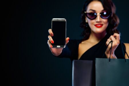 Black Friday and Cyber Monday sale concept for shop. Shopping woman with smile on face holding bag and pointing on tablet isolated on dark backgroundの写真素材