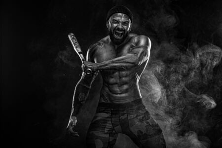 Strong and fit man bodybuilder with baseball bat shows abdominal muscles under a t-shirt. Sporty muscular guy athlete. Sport and fitness concept. Mens fashion.の写真素材