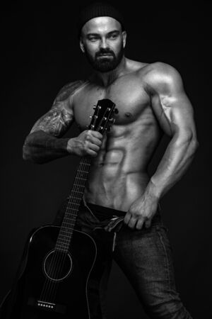 Strong and fit man bodybuilder with guitrar shows abdominal muscles. Sporty muscular guy athlete. Sport and fitness concept. Mens fashion.の写真素材