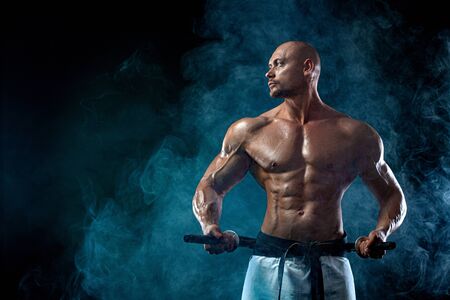 Shirtless man samurai with Japanese sword. Karate fighter on black background with smoke. Handsome and fit man sportsmen bodybuilder physique and athlete. Mens sport motivation.の写真素材