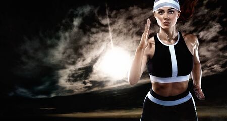 Strong athletic woman sprinter, running on dark background wearing in sportswear. Fitness and sport motivation. Runner concept.の写真素材