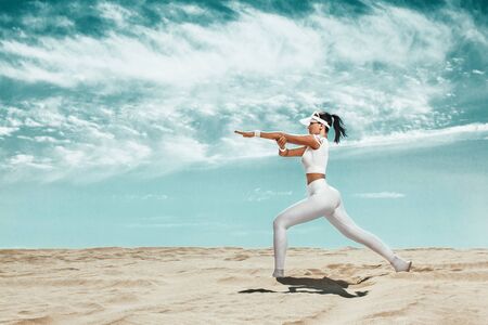 Sporty and fit young woman athlete training at the desert. Cloudy day on coast. The concept of a healthy lifestyle and sport. Woman in white sportswear.の写真素材