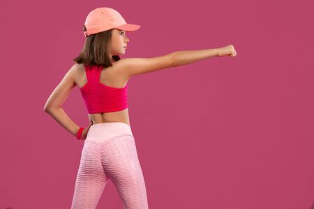 Sports concept. Kid girl doing fitness exercises on green and pink background in sportswear.の写真素材