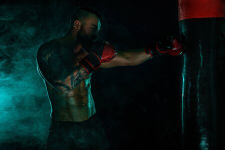 Boxer fighting in gloves with boxing punching bag. Sportsman with tattoos, man Isolated on black background with smoke. Copy Space.の写真素材
