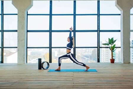 Yoga asana Indoor before a large panoramic window. Sports recreation. Beautiful young woman in yoga pose. Individual sports.の写真素材