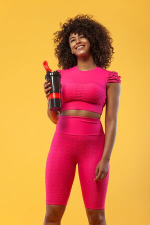 Sporty fit woman, athlete with shaker after fitness exercising on yellow background. Fitness and workout motivation.の写真素材