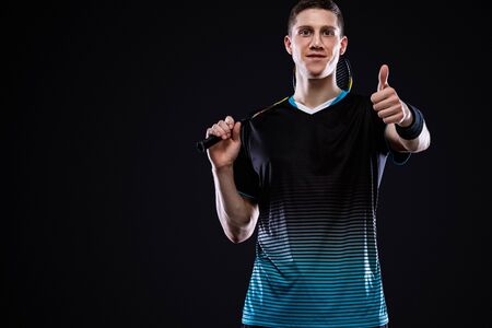 Badminton player in sportswear with racket and shuttlecock on black background. Emotional sport portrait with man which show sight thumbs up and good luck.の写真素材