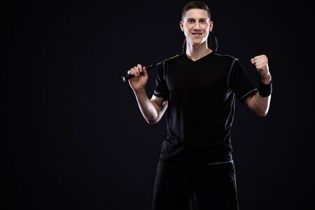 Badminton player in sportswear with racket and shuttlecock on black background. Man celebrates victory on the dark background with.の写真素材