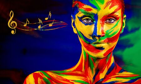 Color art face of woman for inspiration with music notes. Closeup portrait of the bright beautiful girl with colorful make-up and bodyart.の写真素材