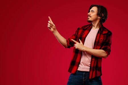 Portrait of happy bearded man with beard pointing finger up at copyspace isolated over red background. Guy in blue sunglasses pick on great idea.の写真素材