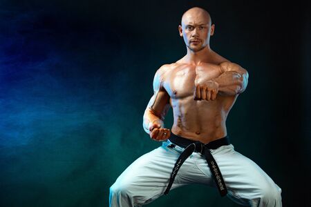 Karate or taekwondo fighter on black background with smoke. Fit man sportsmen bodybuilder physique and athlete. Mens sport motivation.の写真素材