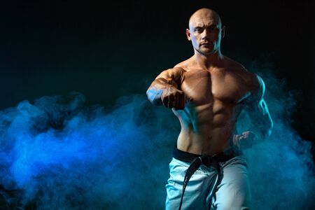 Karate or taekwondo fighter on black background with smoke. Fit man sportsmen bodybuilder physique and athlete. Mens sport motivation.の写真素材